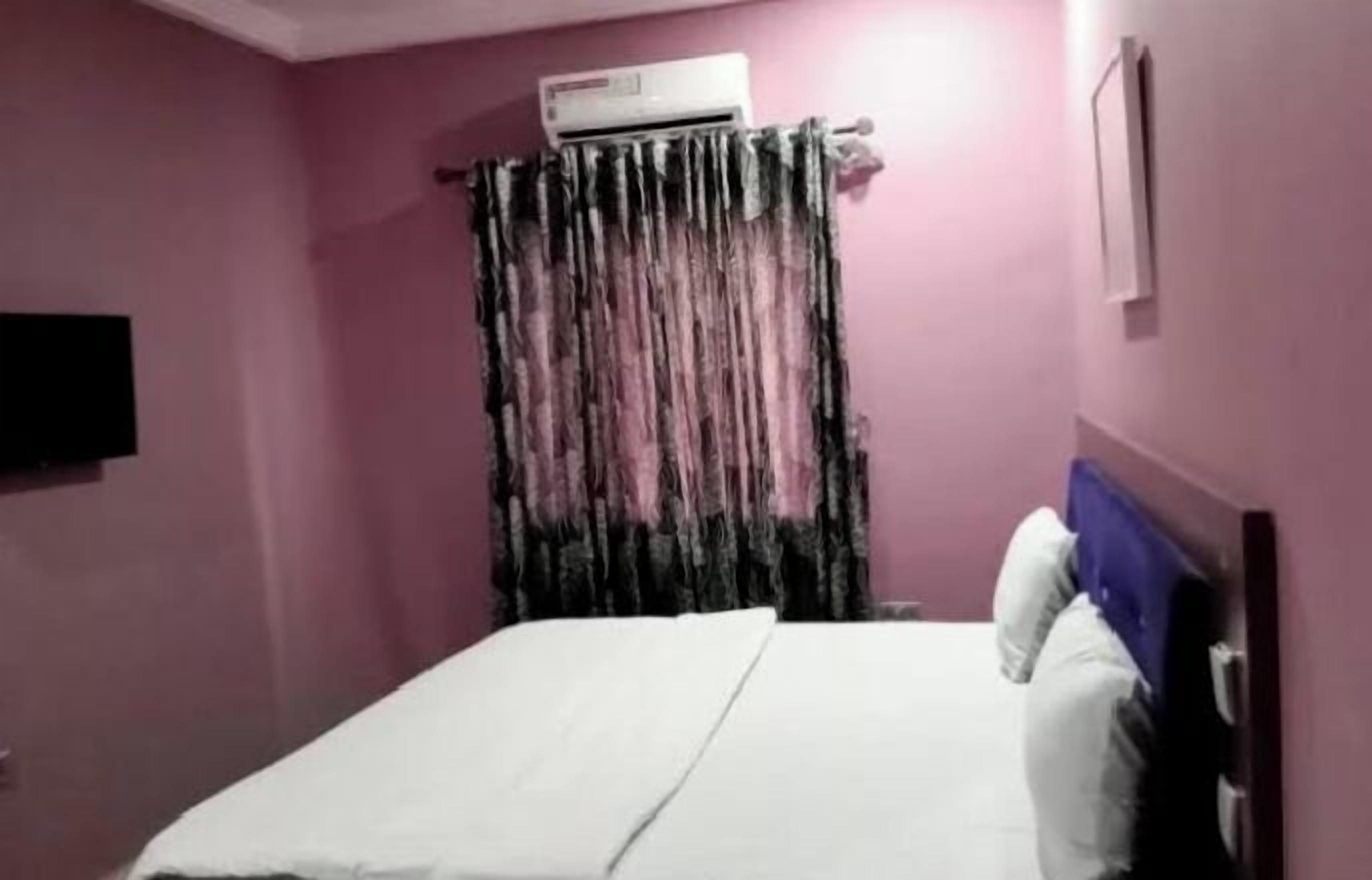 A room with a bed, an air conditioner, and a curtain.