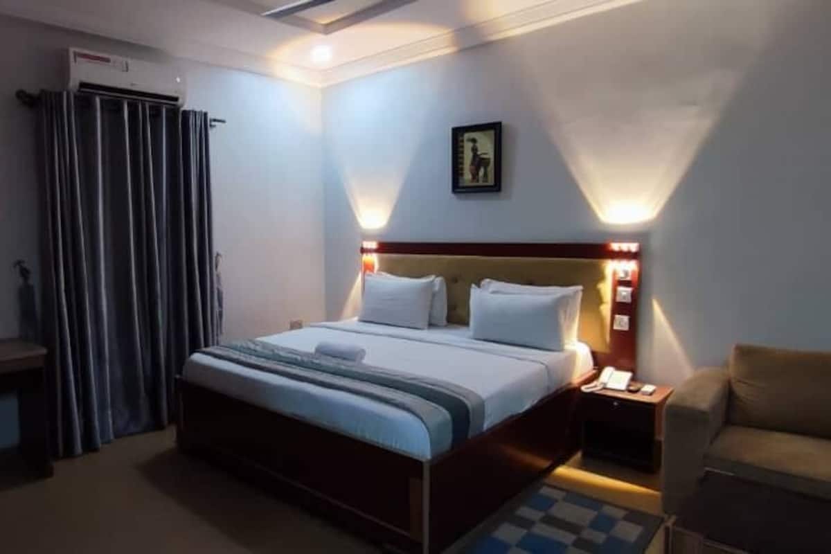 Una habitación de hotel con una cama, mesita de noche, silla y escritorio con otra silla.