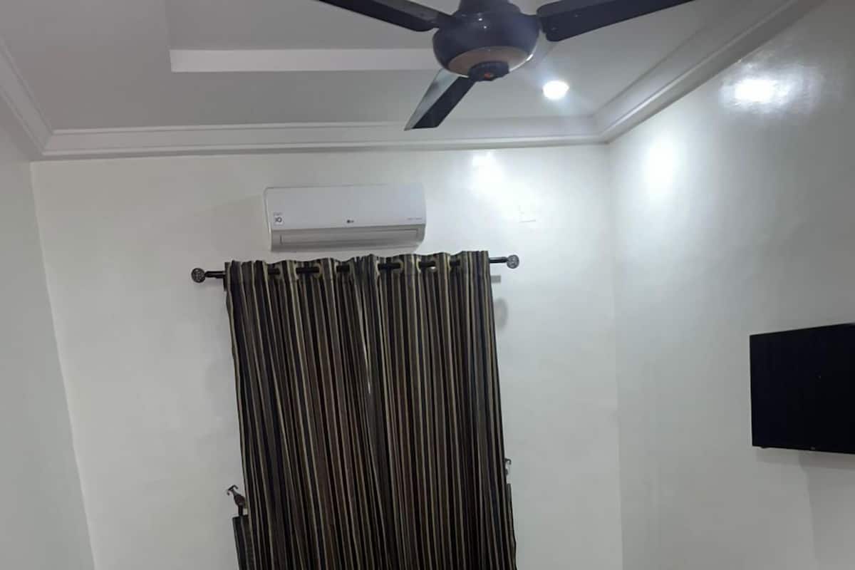 Una sala de estar con dos sofás, una mesa de centro, un ventilador de techo y un televisor montado.