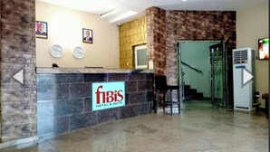 A hotel reception area with a reception desk, framed pictures on the wall, a staircase, and an air conditioning unit. - Fibis Hotel (Lekki)