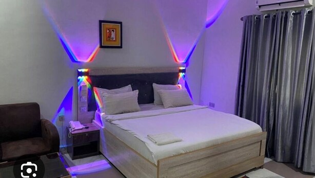 A neatly arranged bedroom with a bed, bedside table, and a chair. - Fibis Hotel (Lekki)
