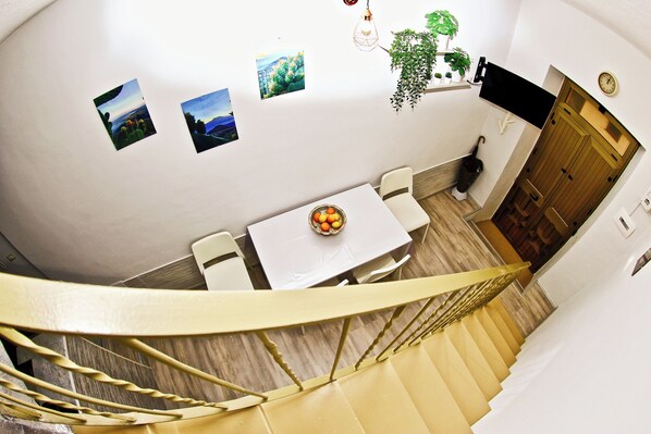 Una escalera conduce a un comedor con una mesa, sillas, un frutero y cuadros en la pared.