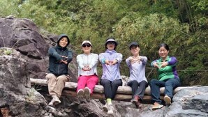 Five people sitting on a wooden bench in a natural setting with rocks and greenery. - Jixi Huihanggudao Cuizhu Mountain Villa (Jixi)