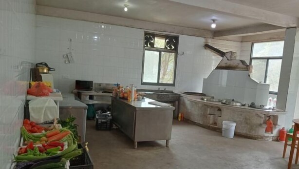 A kitchen with white tiled walls, a sink, and a countertop. There are vegetables on the left side and various kitchen items on the right. - Jixi Huihanggudao Cuizhu Mountain Villa (Jixi)