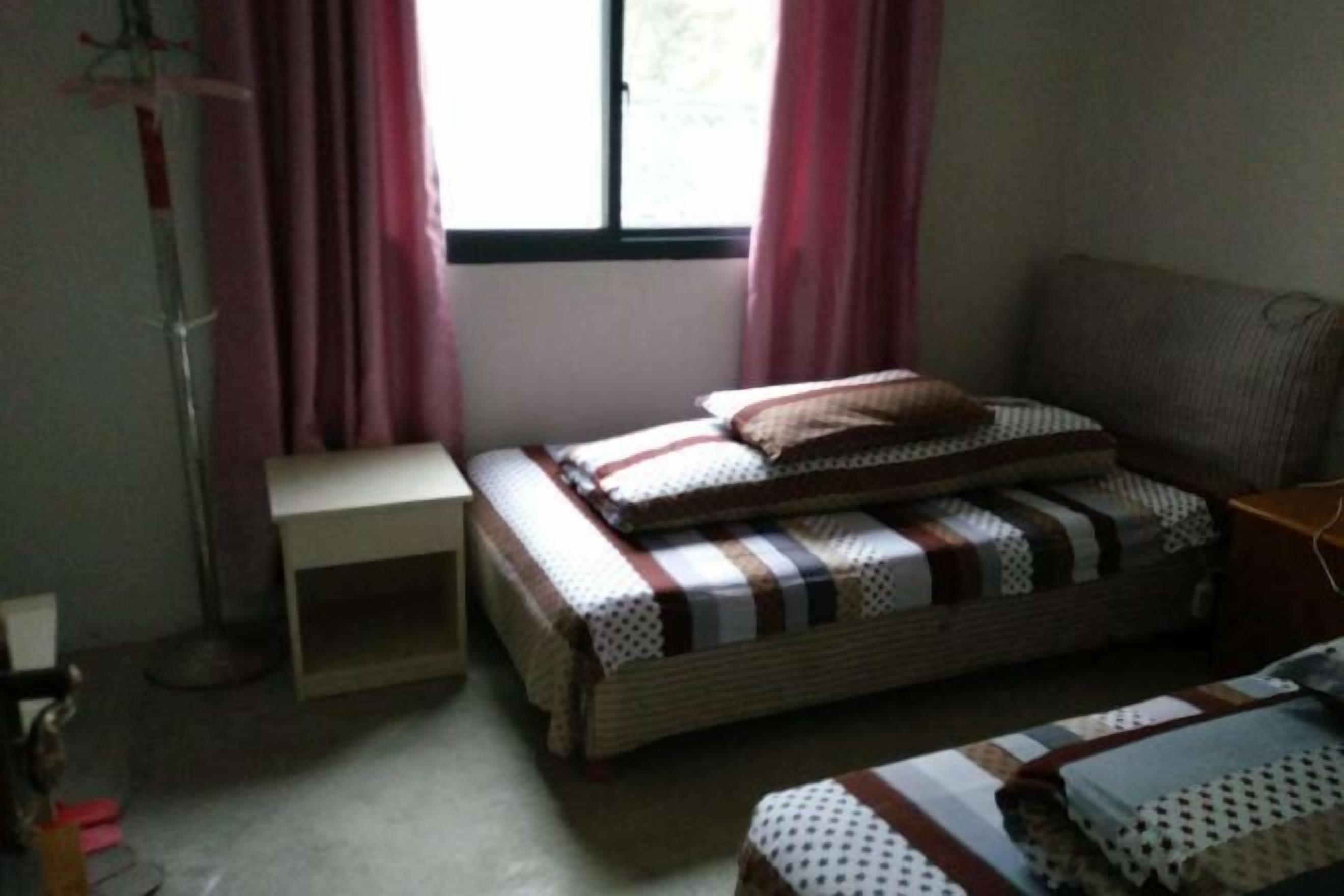 Een kleine, knusse kamer met een enkel bed, een nachtkastje en een raam met gordijnen.