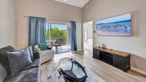 Ein großzügiges Wohnzimmer mit Sofa, Couchtisch, Fernseher und einem Balkon mit Blick auf den Strand.