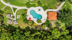 Eine Vogelperspektive zeigt ein Resort mit einem zentralen Schwimmbecken, Liegebereichen und einem Gebäude mit einem Ziegeldach.