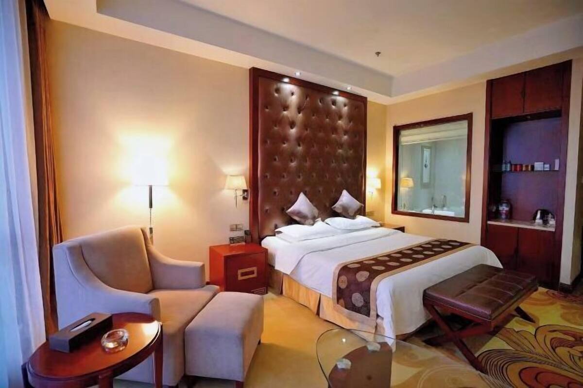 A hotel room with a large bed, a sofa, a small table, a bench, and a wardrobe.