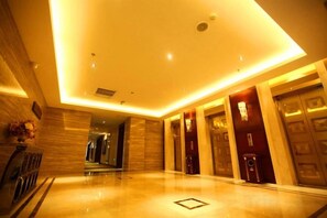 Un vestíbulo de hotel con piso pulido, una recepción y una escalera que lleva a un nivel superior.
