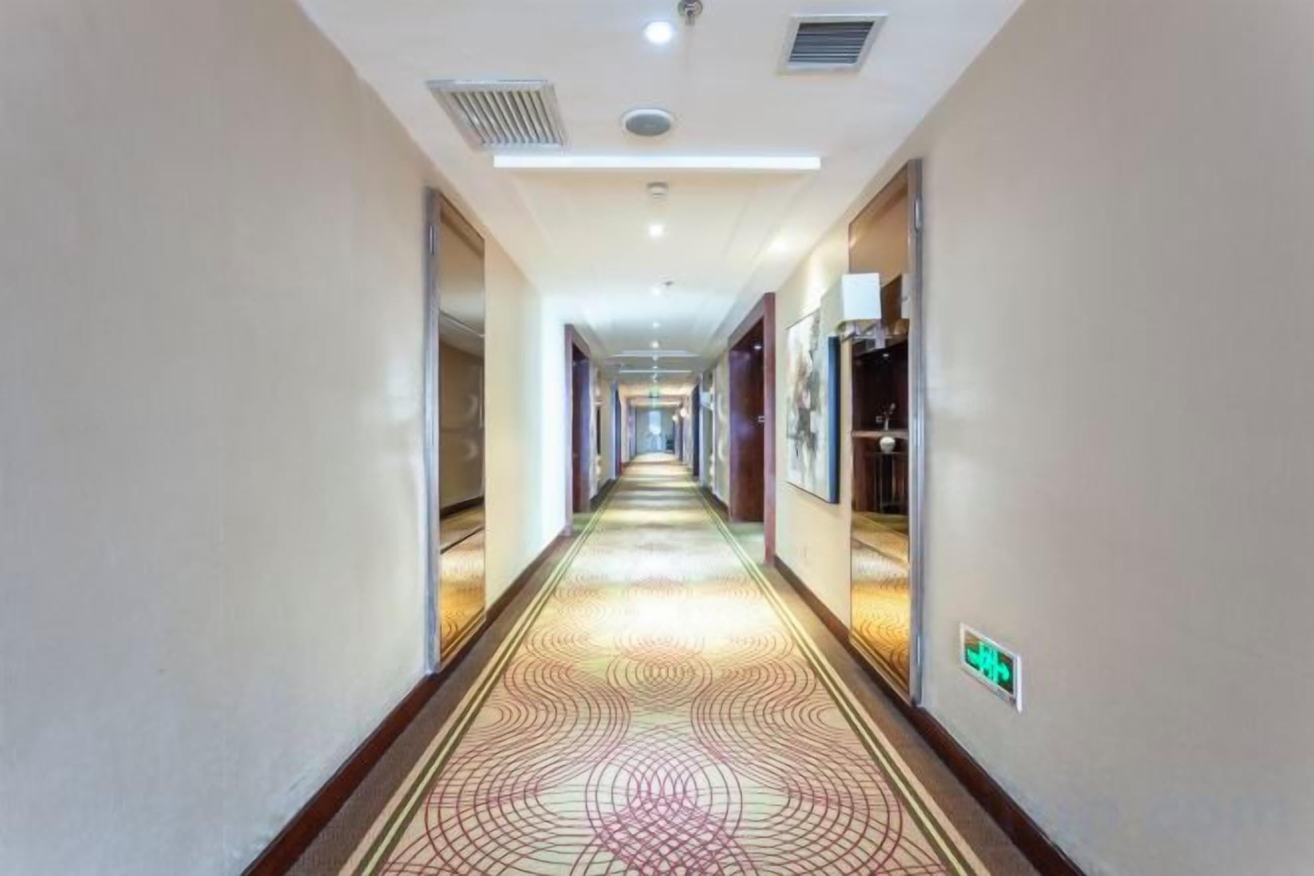 Un couloir d’hôtel avec un tapis à motifs, des portes des deux côtés et un panneau sur le mur de droite.