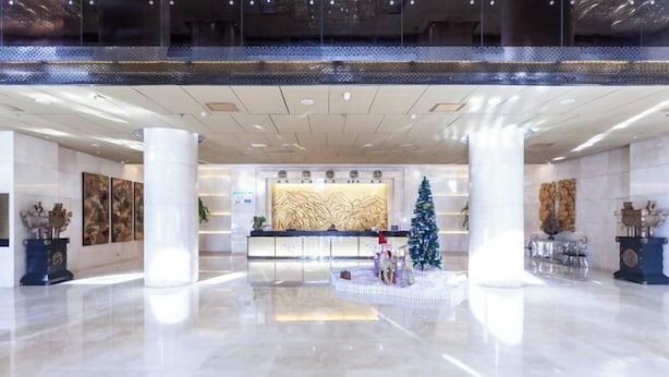 A spacious lobby with a reception desk, large columns, and a Christmas tree. - Yuchenyuan Hotel (Shuozhou)