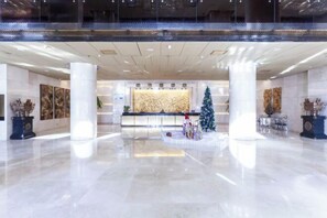 Un vestíbulo espacioso con una mesa de recepción, grandes columnas y un árbol de Navidad.