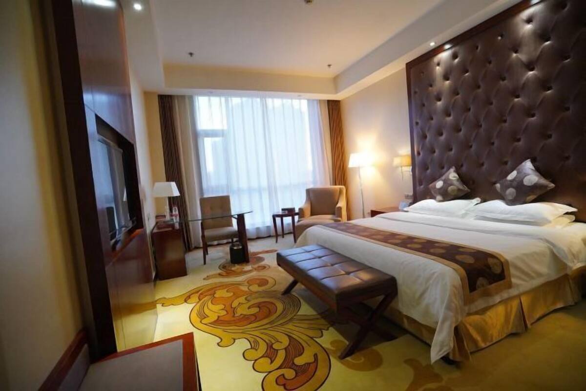 A hotel room with a large bed, a seating area with a bench, a desk, and a chair.