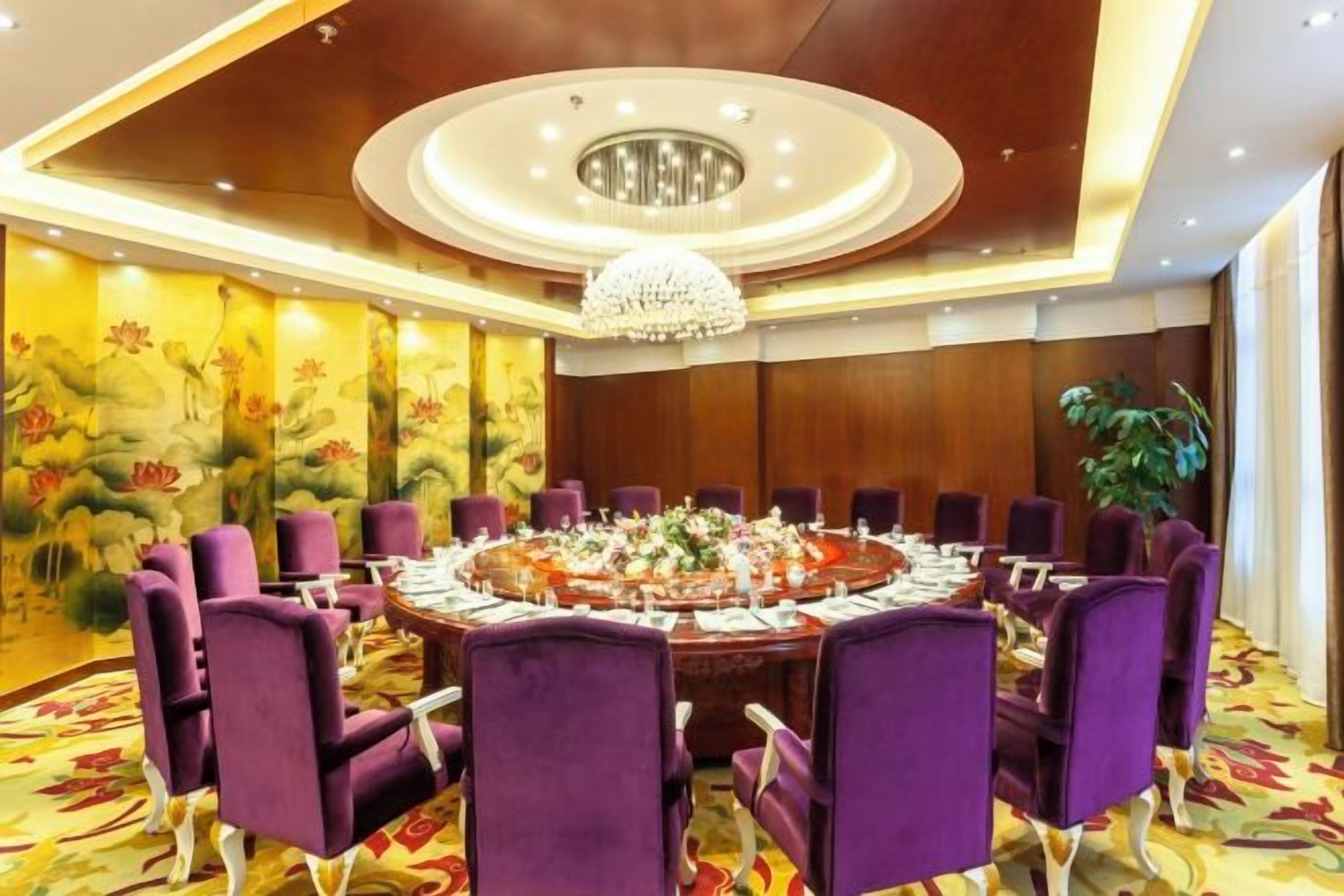 Une salle de conférence avec une table ronde, des chaises violettes et un lustre.