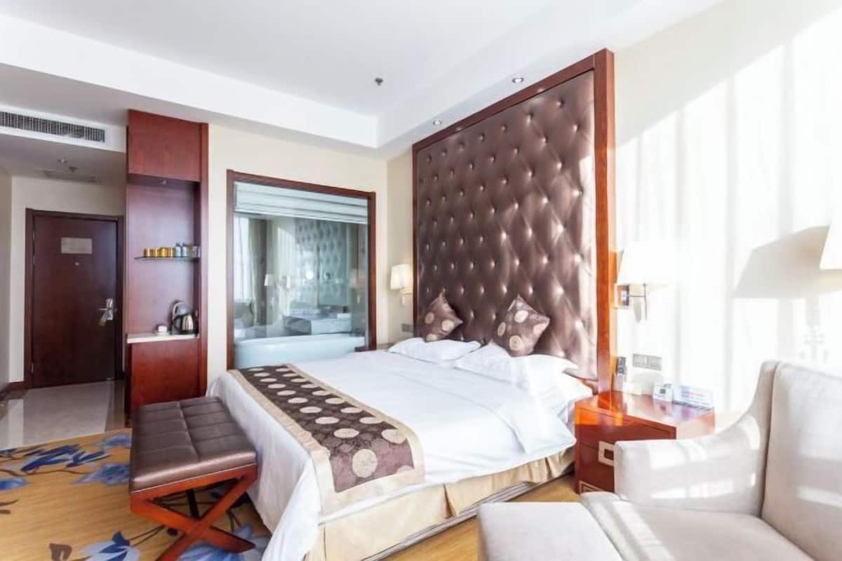 A hotel room with a bed, a bench, a desk, a chair, a window, and a door.