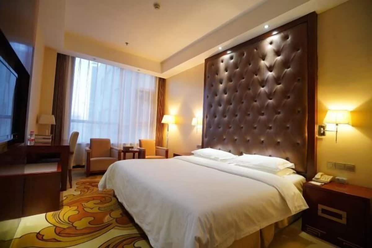 A hotel room with a large bed, a desk, a chair, a TV, and a window with curtains.