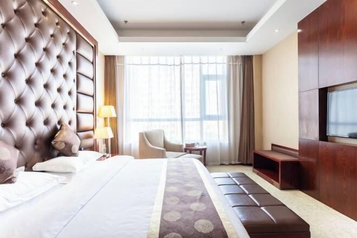 A hotel room with a large bed, a TV, a seating area, and a window with curtains.