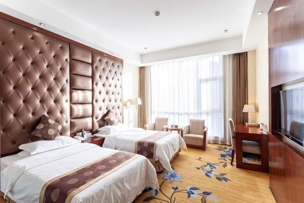 A hotel room with two beds, a large TV, a desk, and a chair.