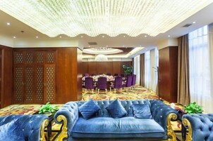 Un hall de hotel con un sofá azul y cómodo, un área de comedor con mesas redondas y un techo decorativo.