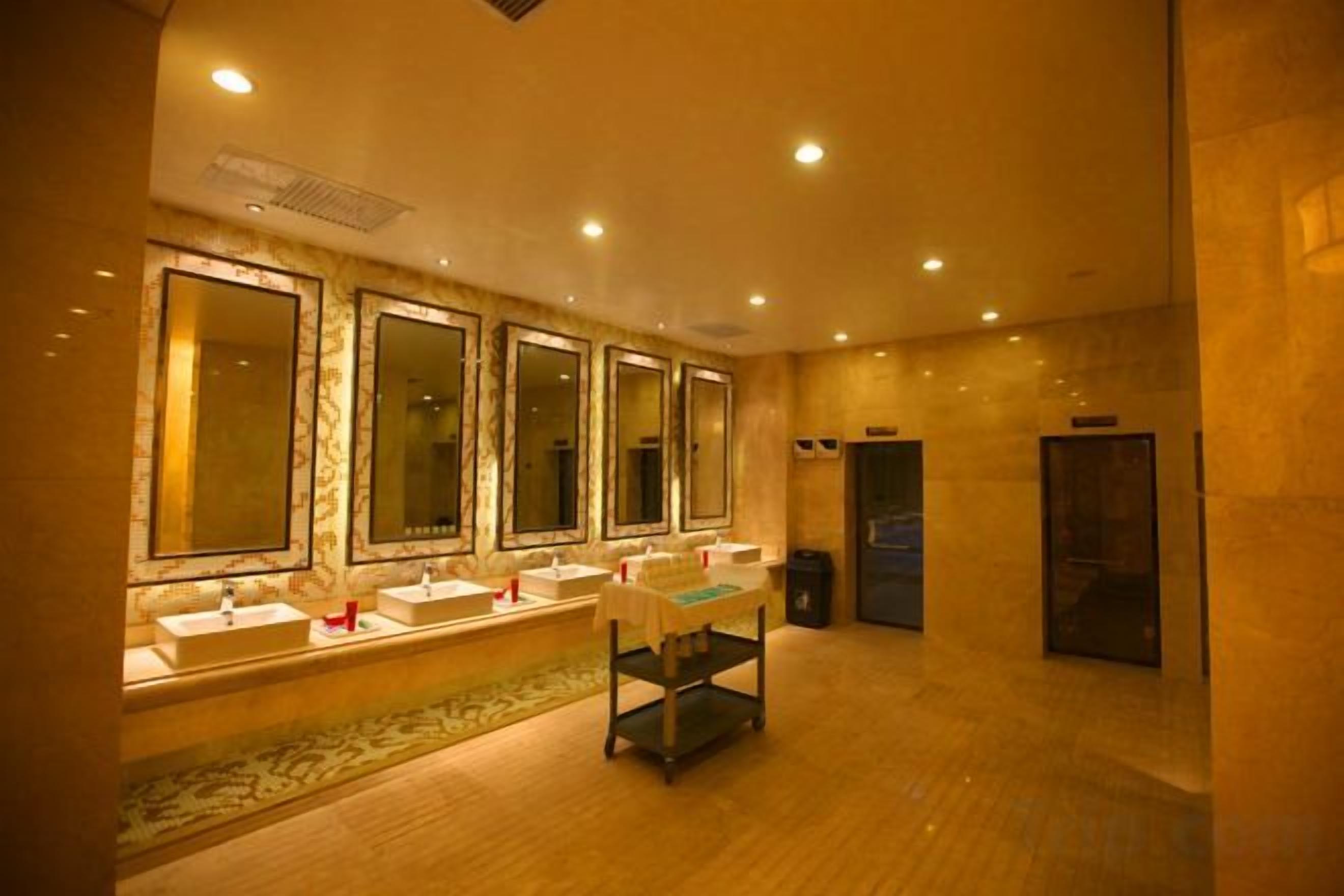 Un baño de hotel con varios lavamanos, espejos y un cesto de basura.