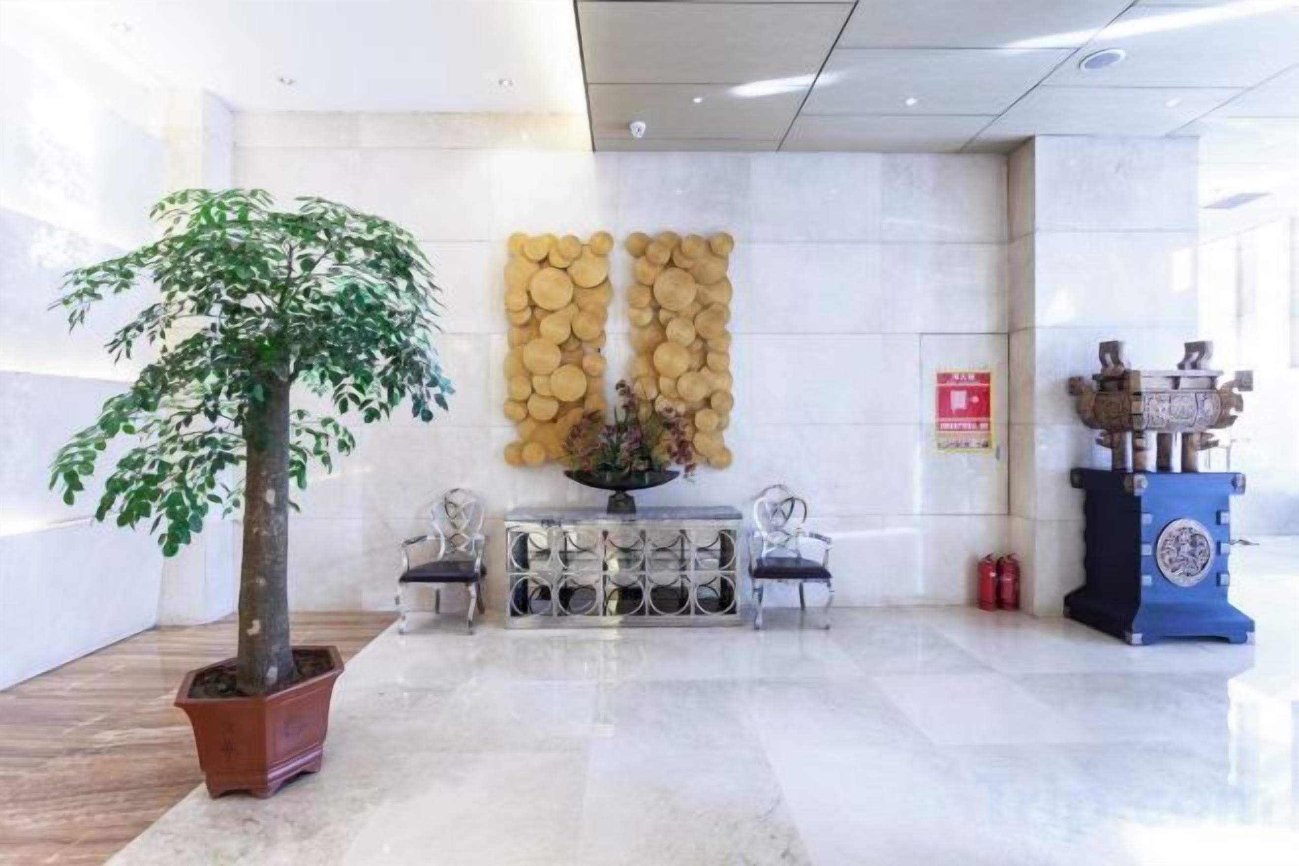 Un espace d’accueil comprenant un arbre en pot, un panneau décoratif fixé au mur, un pupitre bleu et un extincteur.
