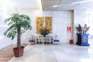 A reception area with a potted tree, a wall-mounted decorative panel, a blue podium, and a fire extinguisher. - Yuchenyuan Hotel (Shuozhou)