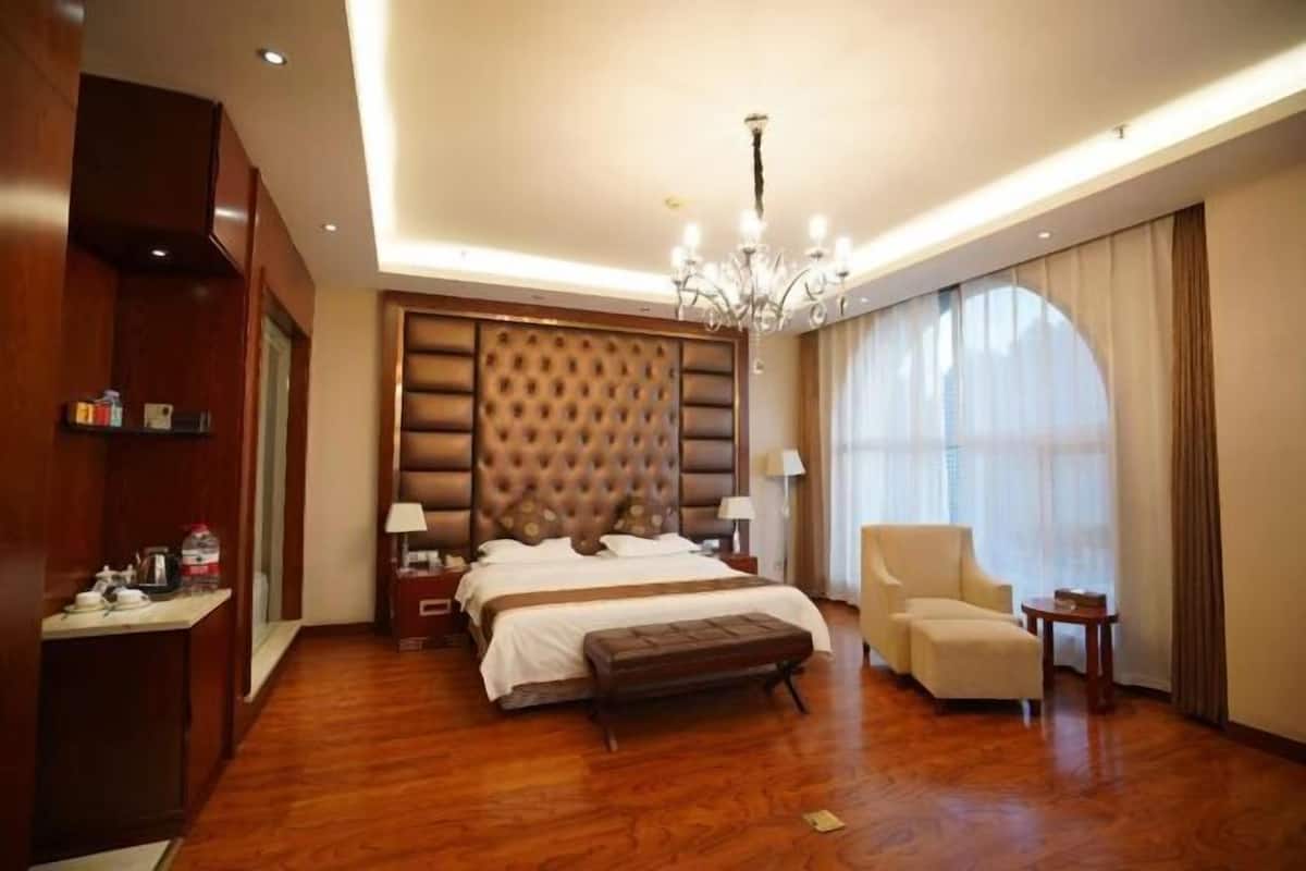 A hotel room with a large bed, a sitting area, a chandelier, and a view of the outdoors.