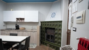 A compact kitchen with white cabinets, a green fireplace, and a dining area with a table and chairs. - Dimora Mariuccia6 paradise nestled in the olive grove, with spa and large outdoor spaces (monte sant'angelo)