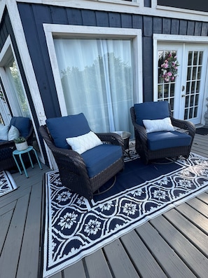 Una terraza con dos sillas de mimbre, una mesita y un tapete estampado.