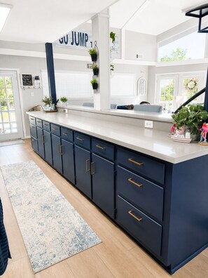 A modern kitchen with dark blue cabinets, a white countertop, and a black ceiling sign.
