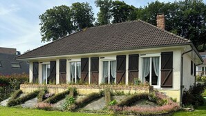A two-story house with a tiled roof, large windows with shutters, and a well-maintained lawn.
