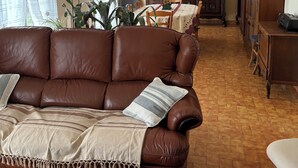 A living room with a brown leather sofa, a wooden coffee table, and a dining area with a wooden table and chairs.