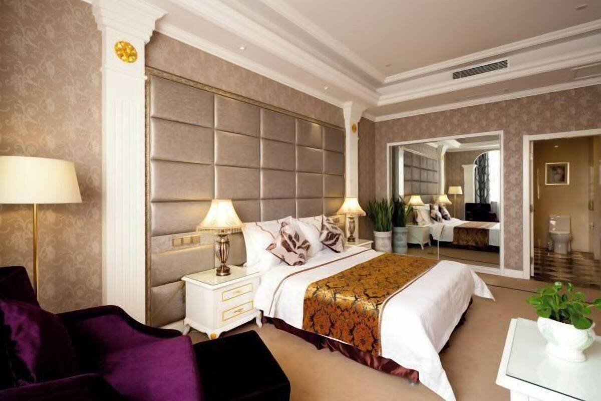 A bedroom with a large bed, two bedside tables with lamps, a mirror, and a view of a bathroom.