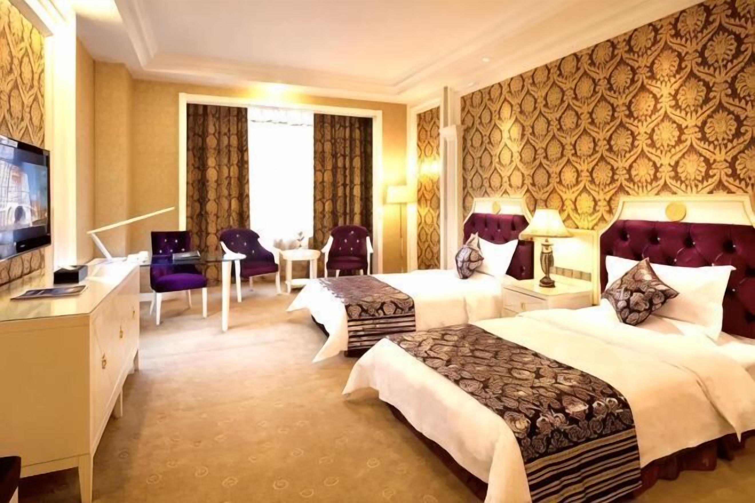 A hotel room with two beds, a desk, a TV, and a chair.