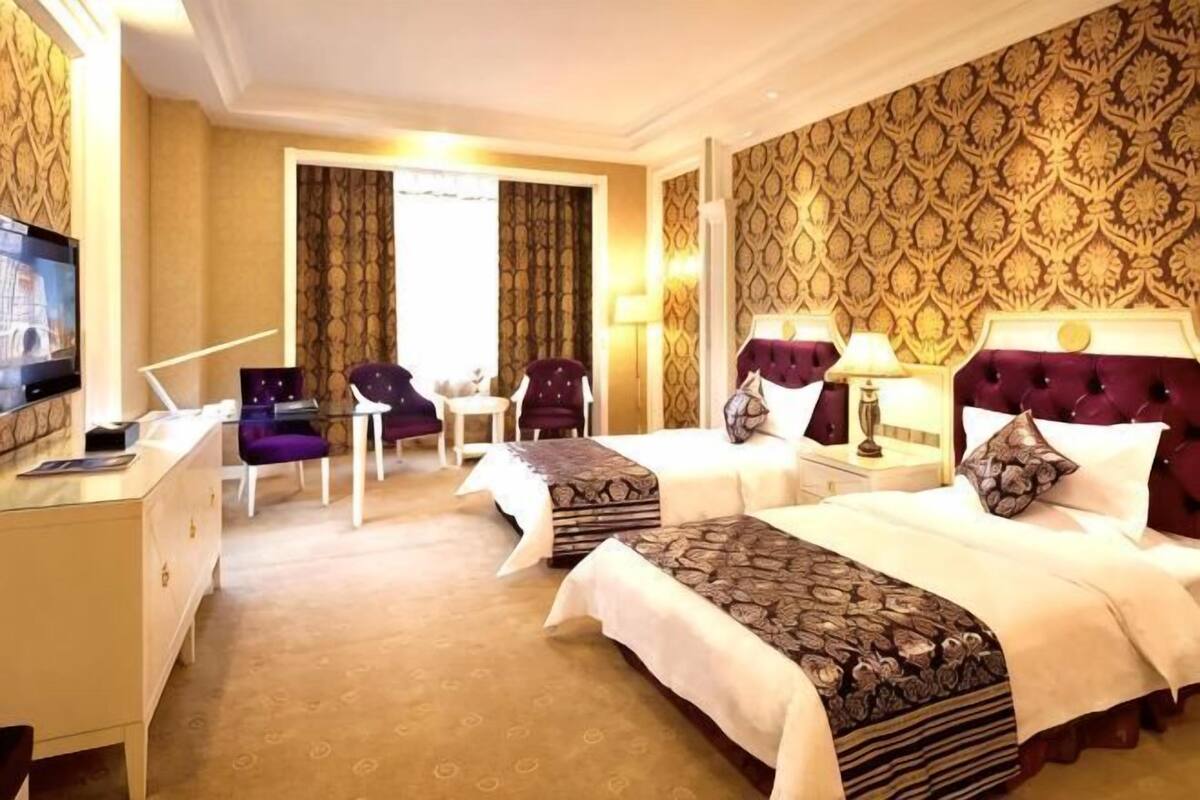 A hotel room with two beds, a desk, a TV, and a chair.