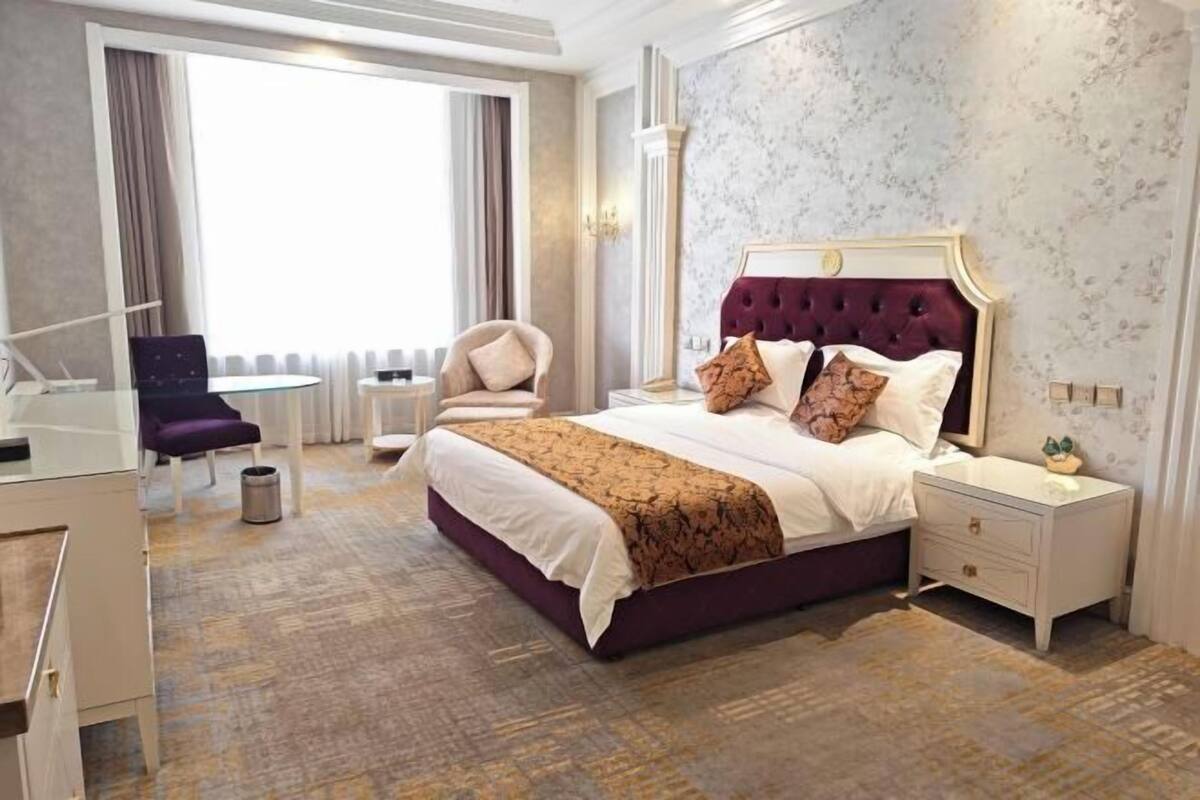 A hotel room with a large bed, a desk, a chair, and a view of the outdoors.