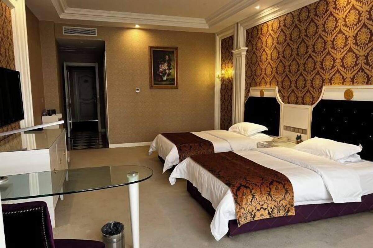 A hotel room with two beds, a glass table, a chair, and a TV.