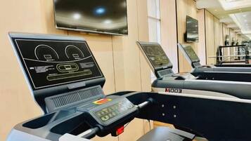 A gym with treadmills and exercise equipment, a television mounted on the wall, and a window providing natural light.