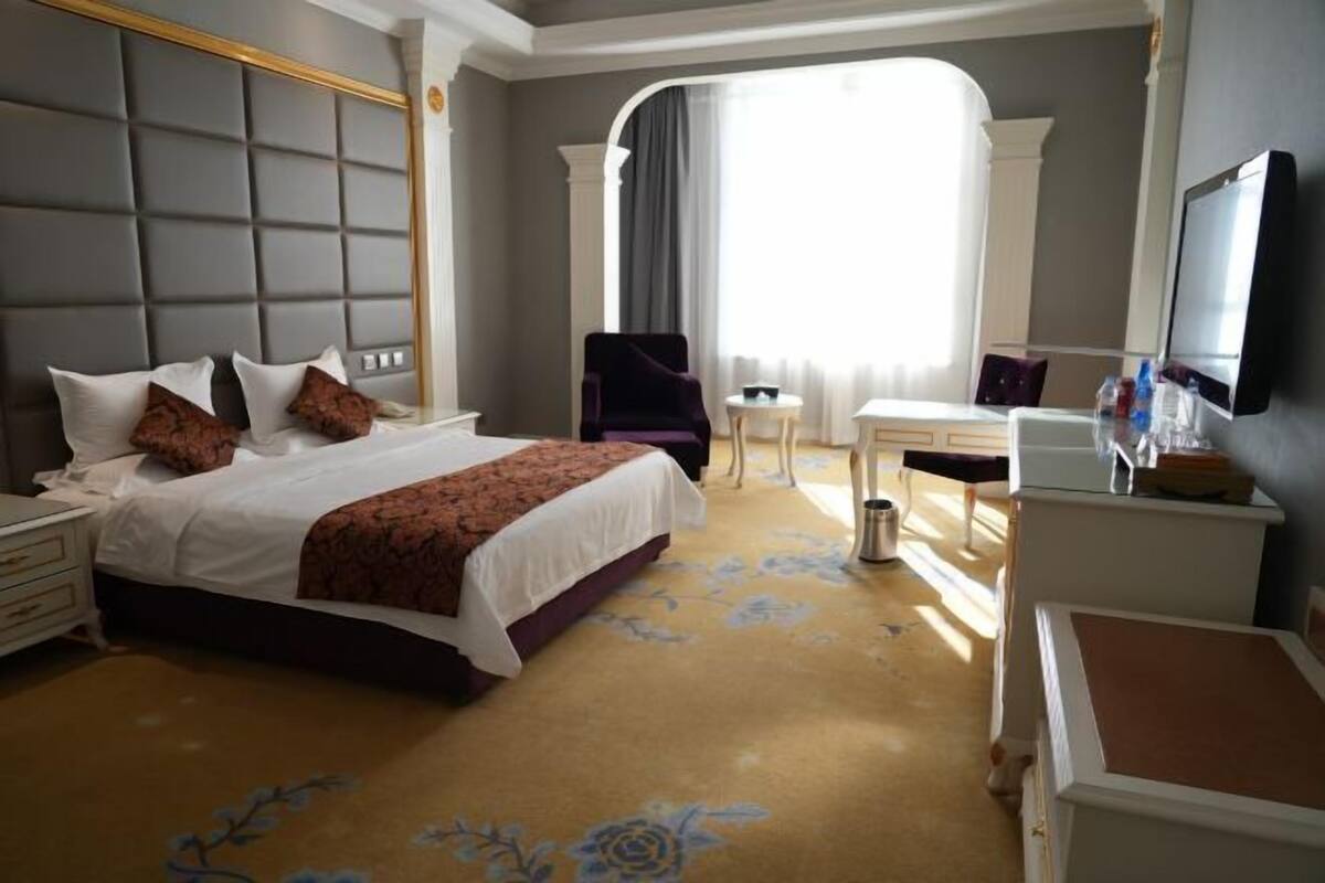 A hotel room with a bed, a desk, a chair, a TV, and a window with curtains.