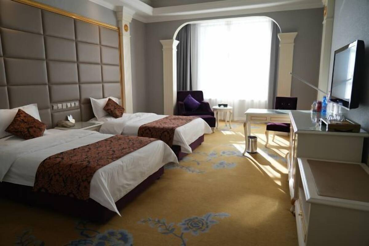 A hotel room with two beds, a desk, a television, and a large window.