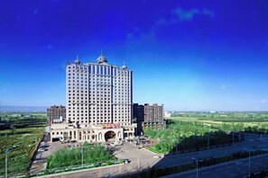 Een hoog hotel met een centrale binnentuin, omringd door groen en een heldere lucht.