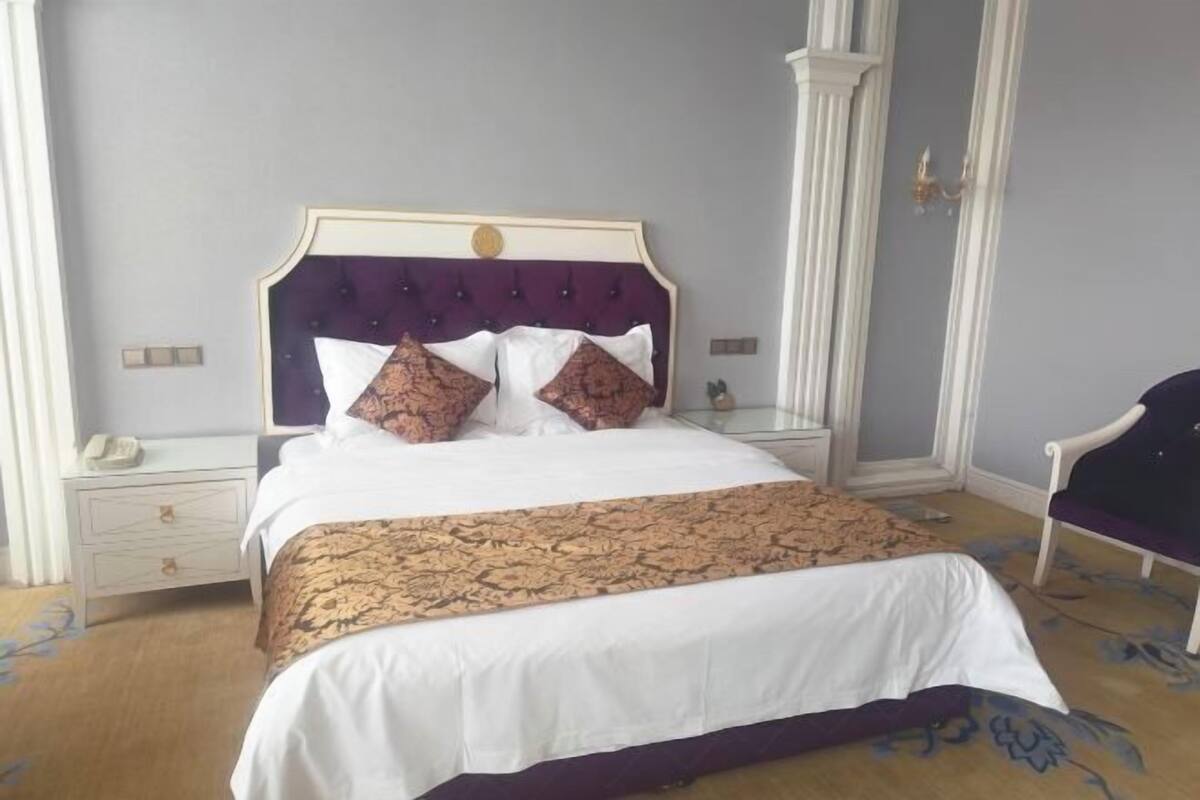 A neatly made bed with a patterned bedspread, a white pillow, and a decorative headboard.