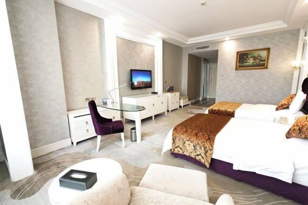 A hotel room with a bed, a desk, a chair, a television, and a painting on the wall.