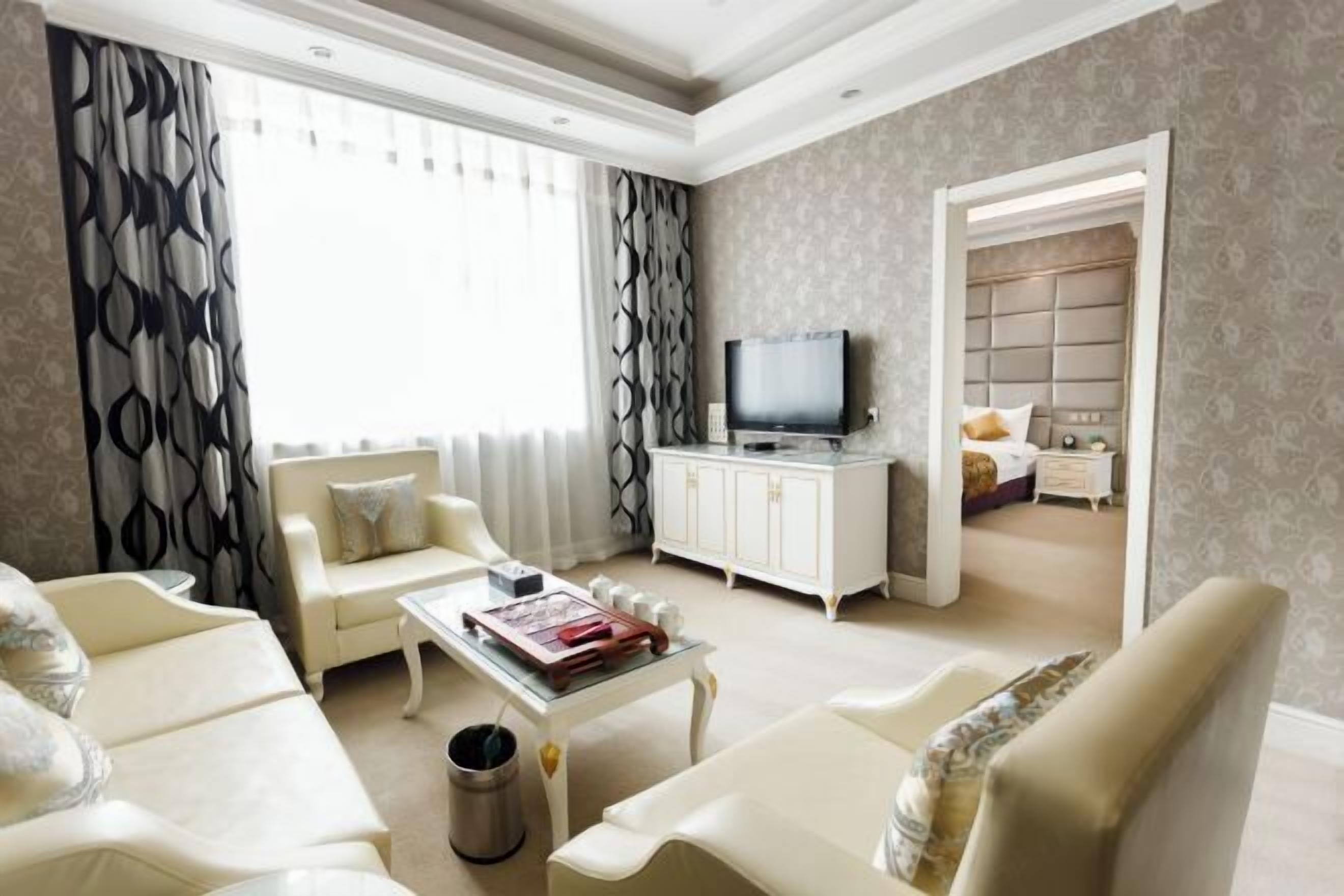 Ein Wohnzimmer mit einer Couch, Sesseln, einem Couchtisch, einem Fernseher und einem Schrank.