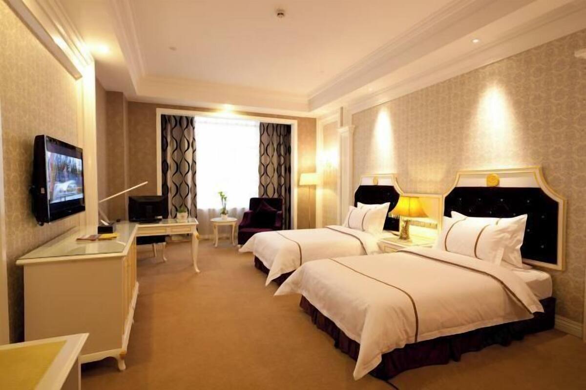 A hotel room with two beds, a TV, a desk, and a chair.