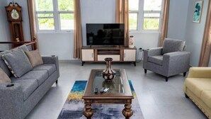 Un salon comprenant un canapé, des fauteuils, une table basse, un téléviseur et une horloge.