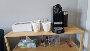Une table en bois avec une machine à café, deux tasses blanches, une boîte et un paquet de mouchoirs.