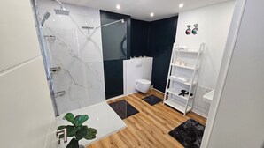 Une salle de bain moderne avec une douche à parois de verre, des toilettes blanches et un meuble-lavabo blanc doté d’étagères.