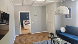 Un salon moderne avec un canapé bleu, une petite table basse sur laquelle se trouve une télécommande, une statuette d’éléphant décorative et un luminaire suspendu.