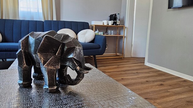 Un salon moderne avec un canapé bleu, une table basse en bois et une sculpture en métal.